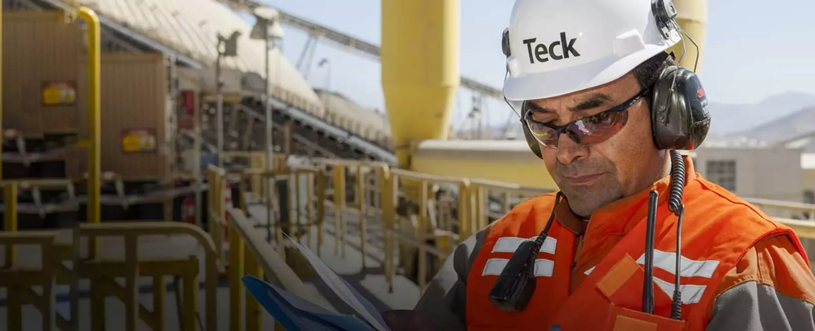 Construction worker in safety gear inspecting machinery and checking documents at a work site.