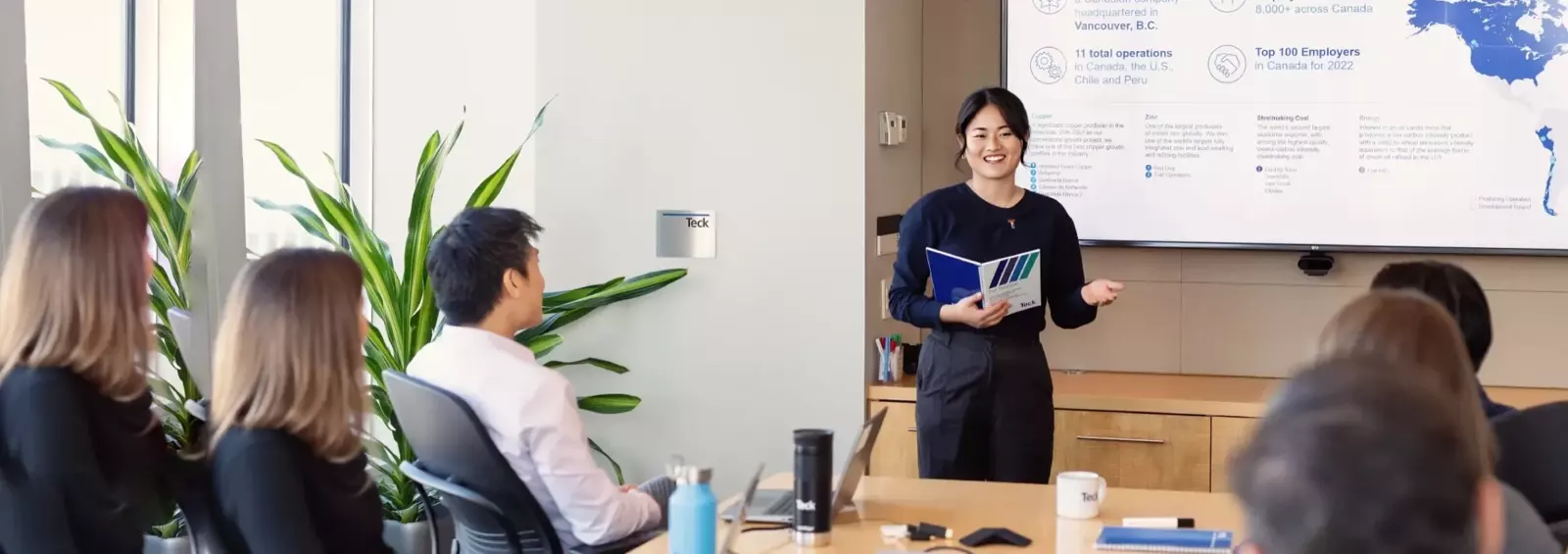 Person presenting to colleagues in a conference room with a projector screen showing data.