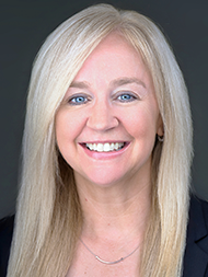 A woman with long blonde hair and a black blazer smiling at the camera.