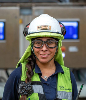 Person in safety gear and helmet smiling at an industrial site.