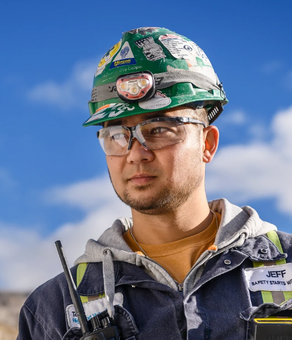 A construction worker wearing safety gear, including a helmet and glasses, stands outdoors.