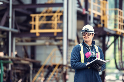 Engineer with hard hat and clipboard at industrial site.