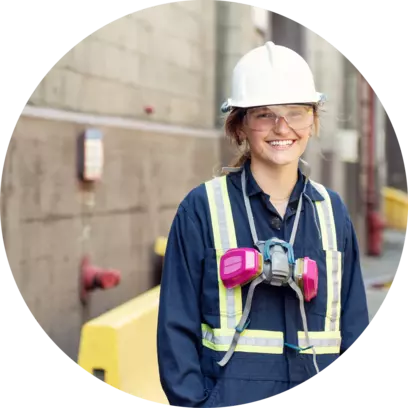 Smiling construction worker in safety gear and hard hat standing outside a building.