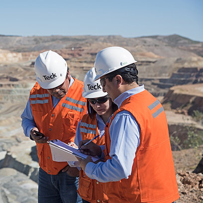 Three workers in safety vests discuss paperwork at a mining site.