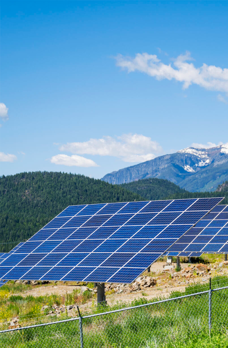 Solar panels in a field with mountains and blue sky in the background.