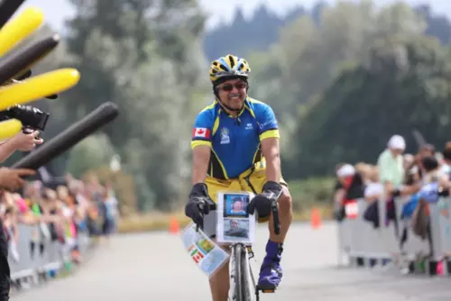 Cyclist in a race, wearing a blue and yellow helmet, smiling, with cheering crowd in the background.