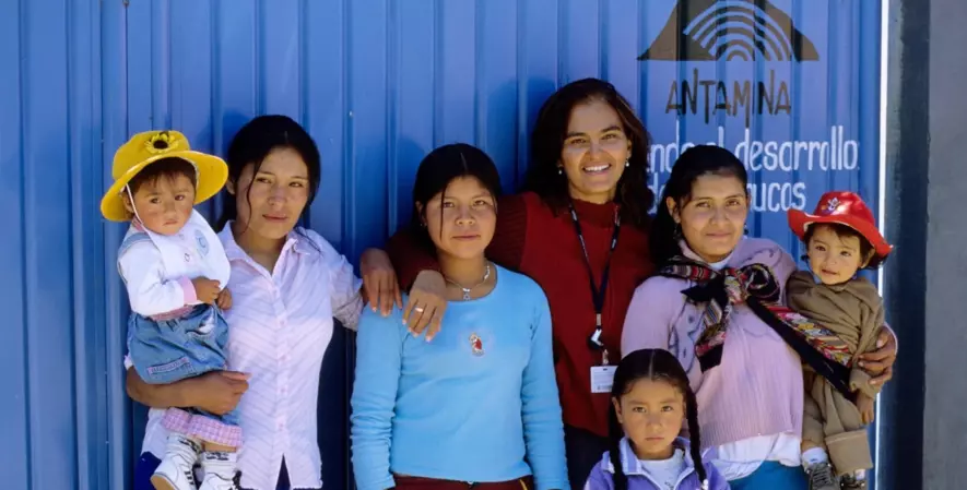 A group of women and children stand smiling in front of a blue building.
