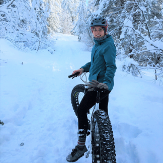 A person in winter clothing rides a fat-tire bike on a snowy forest trail.