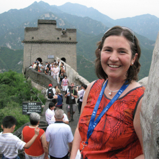 Smiling woman in red top at the Great Wall of China, surrounded by tourists with mountains in background.