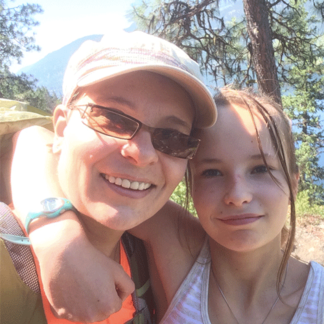 Two people smiling and posing together outdoors, surrounded by trees and mountains.