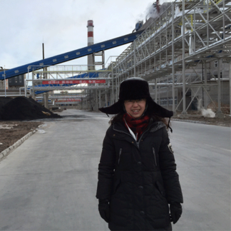 A person in a coat and hat stands on an industrial site with conveyor belts and metal structures.