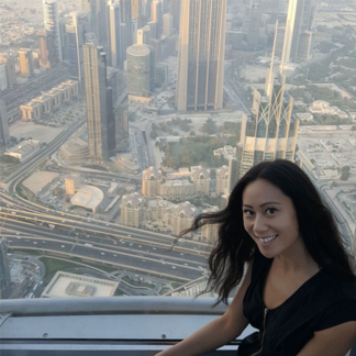 Smiling woman with long hair posing atop a high-rise building with a cityscape in the background.