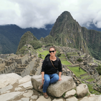 Person sitting on a rock at Machu Picchu with mountains and ancient ruins in the background.