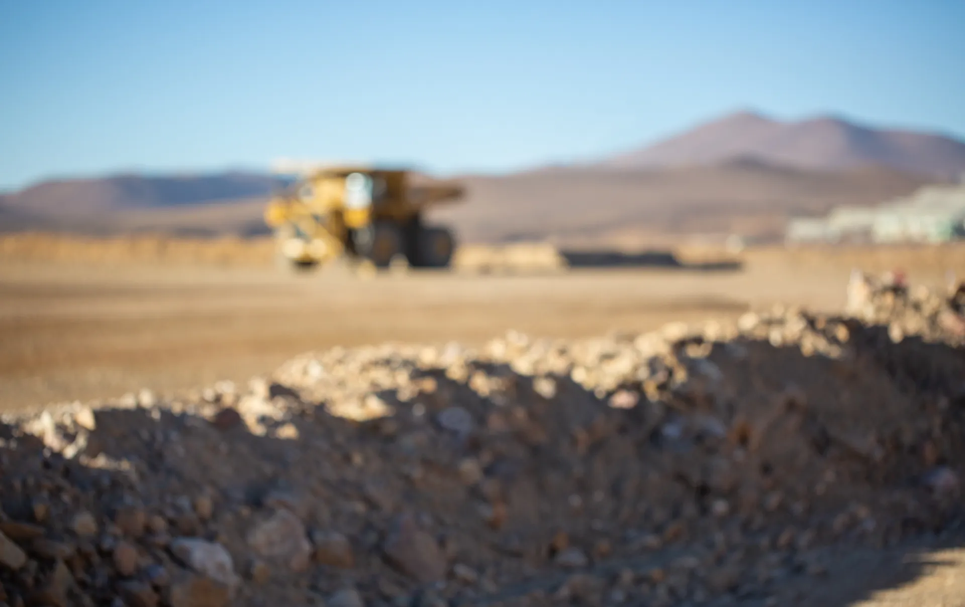 Blurred image of a construction vehicle on a rocky terrain in a desert landscape under a blue sky.