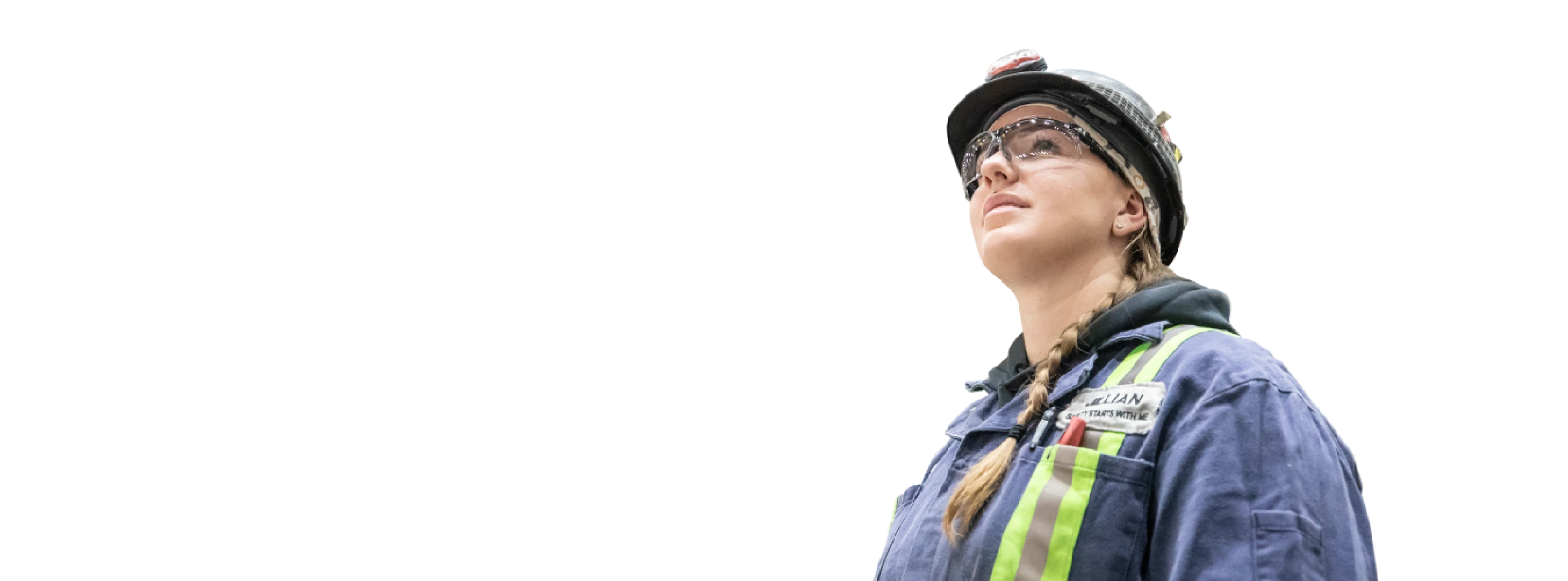 Worker wearing safety gear and a reflective vest, looking up.