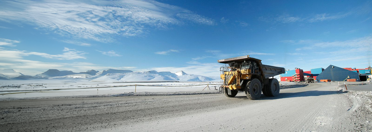 Heavy-duty mining truck in a snowy, mountainous landscape with buildings in the background.